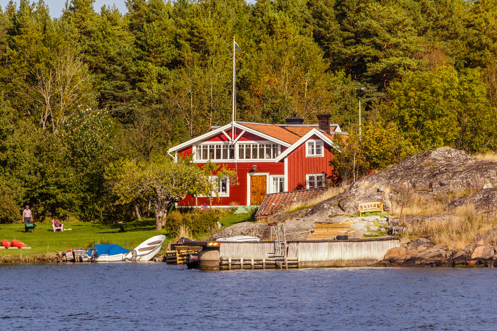 Rødt sommerhus med hvote vinduskarmer ved sjøen med brygge foran