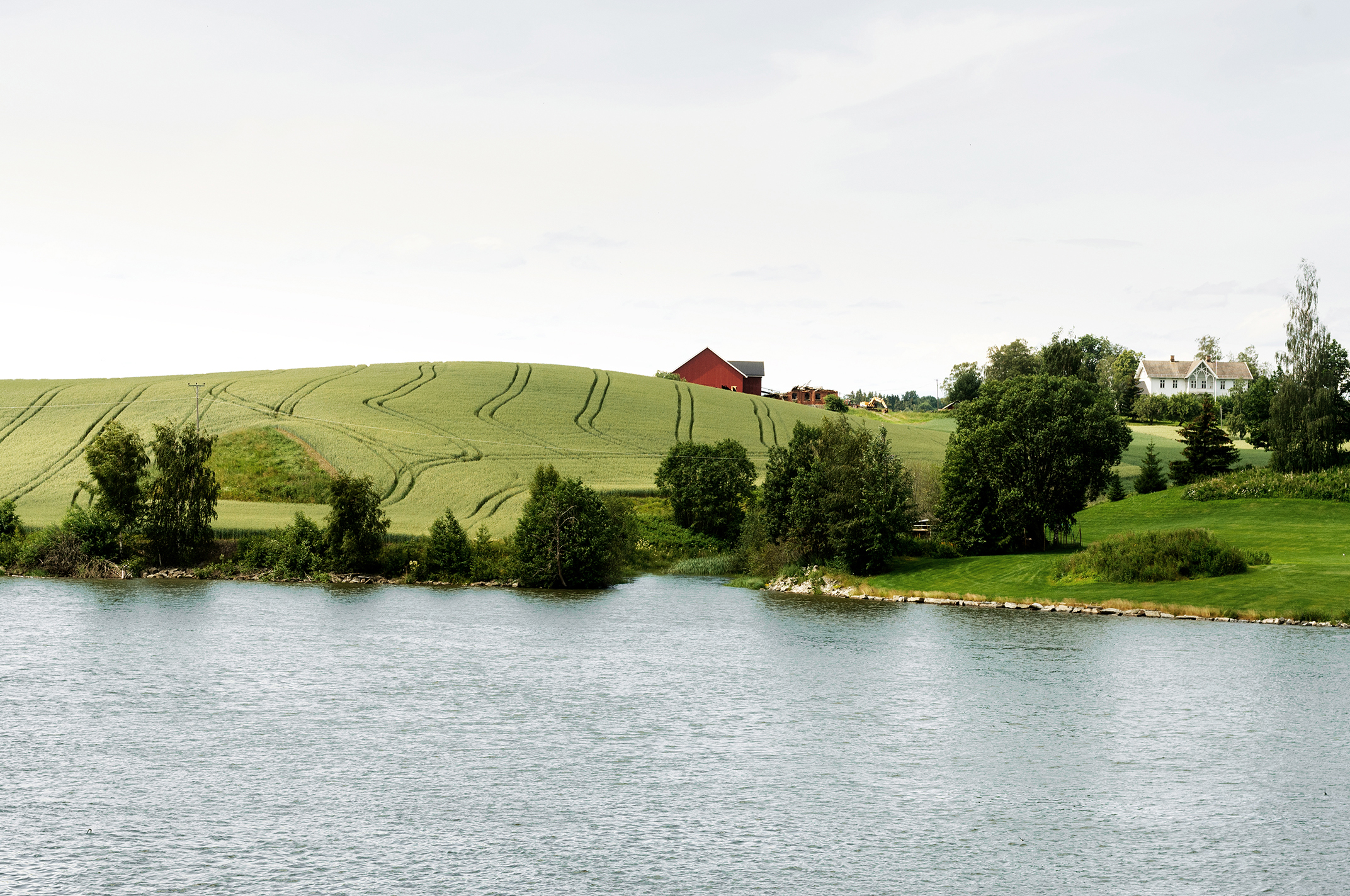 Vann med gårdsbruk og grønne enger i bakgrunnen